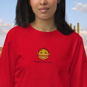 Puede incluir: Sudadera roja de manga larga con una cara amarilla pixelada y el texto "The music is nice here."