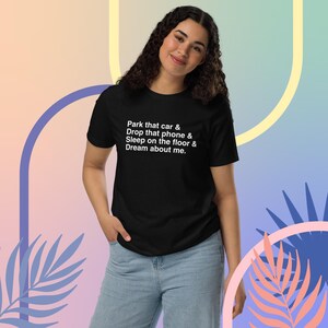 May include: Black t-shirt with the text "Park that car & Drop that phone & Sleep on the floor & Dream about me." The shirt is paired with blue jeans. The background has pastel colours.