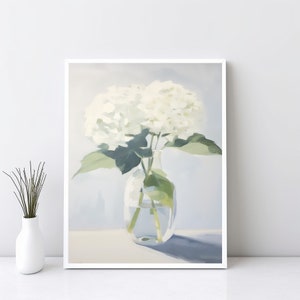 Op de afbeelding: Een wit boeket hortensia's in een heldere glazen vaas tegen een lichtblauwe achtergrond. De hortensia's staan in volle bloei en de vaas staat op een wit oppervlak.