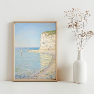Op de afbeelding: Een ingelijst schilderij van een witte klif aan een strand met blauw water en een heldere lucht. Het water is kalm en reflecteert de lucht en de klif. Er zijn een paar kleine figuren op het strand.