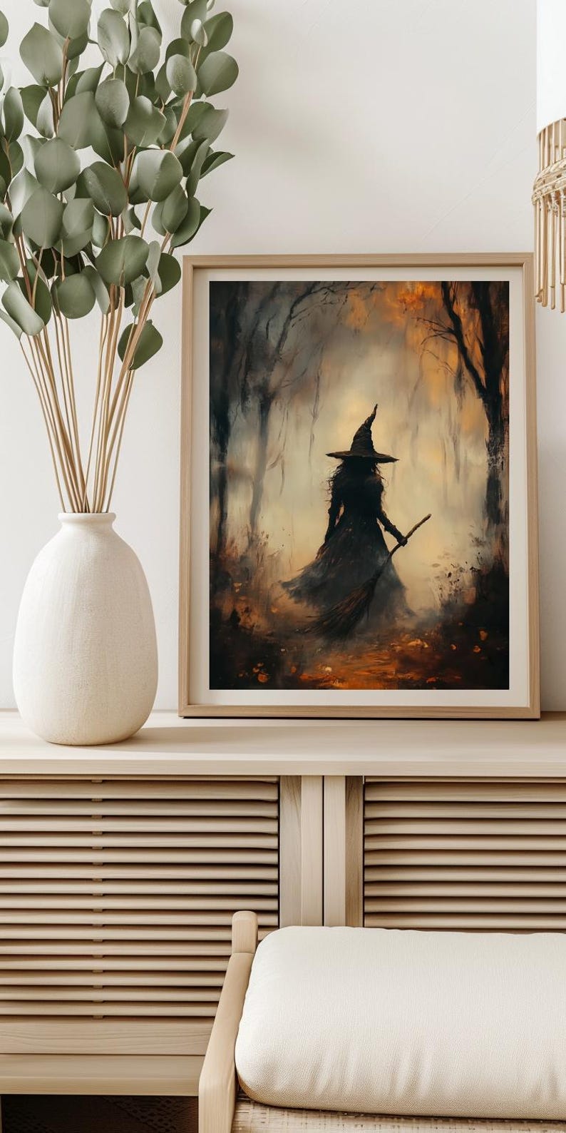 Pu&ograve; includere: Stampa artistica incorniciata raffigurante una strega silhouette in un ambiente forestale. La strega indossa un cappello a punta e tiene una scopa. L'opera d'arte presenta una tavolozza di colori tenui di marroni, arancioni e neri, creando una scena misteriosa e suggestiva.