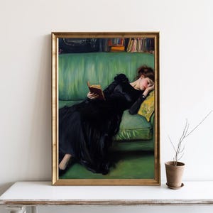 May include: A painting of a woman in a black dress lying on a green sofa, reading a book. The woman is asleep and her head is resting on a yellow cushion. The painting is framed in gold.