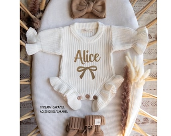 May include: A cream-colored long-sleeve knit romper featuring a ruffled collar and cuffs, with the name Alice and a bow graphic in brown text. Includes a matching brown fabric headband and a pair of brown knit booties with a small white label.