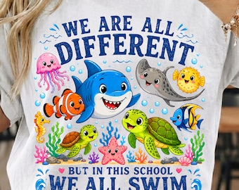 May include: A white t-shirt featuring a colorful graphic of various sea creatures including a shark, sea turtles, a jellyfish, a stingray, and fish. The text reads, "WE ARE ALL DIFFERENT BUT IN THIS SCHOOL WE ALL SWIM TOGETHER" in blue letters.