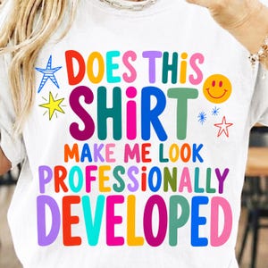 Op de afbeelding: Een wit t-shirt met kleurrijke tekst in verschillende lettertypes met de tekst: "DOES THIS SHIRT MAKE ME LOOK PROFESSIONALLY DEVELOPED". Het ontwerp bevat diverse grafische elementen zoals een blauwe gestreepte ster, een gele ster, een geel smileygezicht en kleine rode en blauwe sterren.