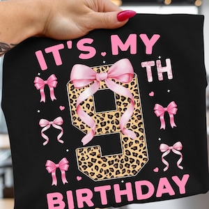 May include: Black t-shirt with the text "IT'S MY 9TH BIRTHDAY" in pink. The number 9 is leopard print with a pink bow. Pink bows and hearts are scattered around the number. A fun birthday shirt.