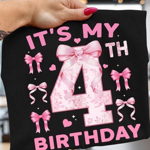 Könnte beinhalten: Schwarzes T-Shirt mit dem Text "IT'S MY 4TH BIRTHDAY" in Pink. Die Zahl 4 ist mit einem floralen Muster und einer großen rosa Schleife verziert. Zusätzliche rosa Schleifen und Herzen sind um das Design verstreut.