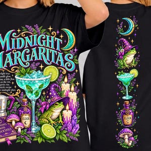 Puede incluir: Una camiseta negra con un estampado gráfico que incluye el texto "Midnight Margaritas". El diseño muestra una rana verde con un sombrero de bruja morado, una copa de margarita, una botella de elixir morada, velas, setas y un libro titulado "Potions and Cocktails".