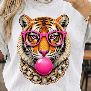 Könnte beinhalten: Weißes T-Shirt mit einem Tigergesicht-Design, das eine rosa Brille und eine Kaugummiblase trägt. Der Tiger hat orange und schwarze Streifen, eine rosa Nase und eine goldene Halskette mit Diamantbesatz.