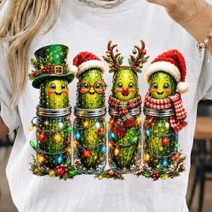 Peut inclure: Un t-shirt blanc avec un motif de quatre cornichons verts dans des bocaux en verre. Les cornichons sont décorés pour les fêtes avec un haut-de-forme vert, un bonnet de Père Noël rouge avec des lunettes, des bois de renne et un bonnet rouge.