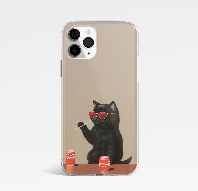 Pu&ograve; includere: Una custodia per telefono trasparente con un gatto nero che indossa occhiali da sole rossi e tiene una cannuccia. Il gatto &egrave; seduto su un tavolo con due lattine di Coca-Cola rosse e bianche.