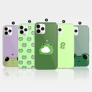 May include: Five different phone cases with frog designs. The cases are all green and feature different frog illustrations. One case has a purple background with a frog and a heart.