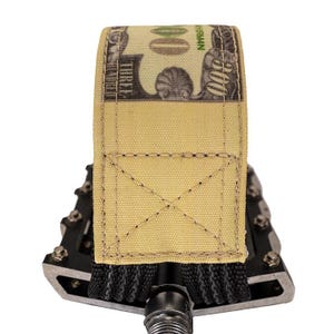Puede incluir: Una correa de tela color beige con un dise&ntilde;o de billete de 100 $, cosida con un patr&oacute;n de cruz, est&aacute; envuelta alrededor de un pedal de bicicleta negro. El pedal tiene un marco de metal plateado y un agarre negro.