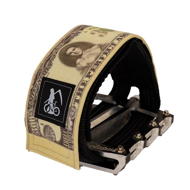 Puede incluir: Una correa de pedal de bicicleta con un dise&ntilde;o que se asemeja a un billete de 100 d&oacute;lares estadounidenses. La correa tiene un interior negro y un peque&ntilde;o cuadrado negro con un gr&aacute;fico blanco de una bicicleta y una guada&ntilde;a. El texto "THE PERFECT AS" est&aacute; impreso en la correa.