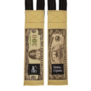 Puede incluir: Dos correas de tela beige con un dise&ntilde;o que se asemeja a un billete de $300. Las correas presentan el texto "THE PERFECT ASS" y "Пеппа и Стрэпа". Cada correa tiene un logotipo en blanco y negro de una bicicleta y una guada&ntilde;a.