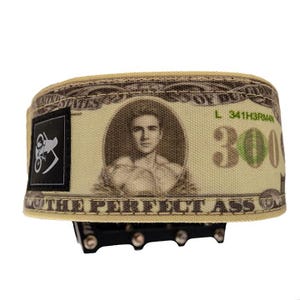Puede incluir: Un pedal de bicicleta beige y verde con un dise&ntilde;o que se asemeja a un billete de 300 $. El billete presenta un retrato y el texto "THE PERFECT ASS". Un logotipo en blanco y negro est&aacute; en el lateral.