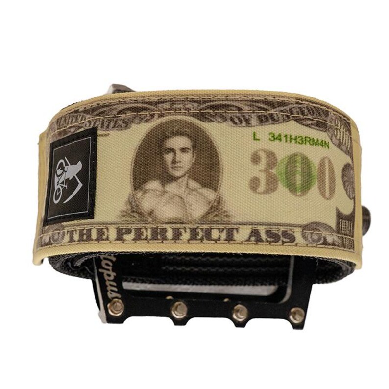 Puede incluir: Un pedal de bicicleta con una correa que presenta un dise&ntilde;o que se asemeja a un billete de 300 $. El dise&ntilde;o del billete incluye un retrato y el texto "THE PERFECT ASS". Un logotipo negro est&aacute; en el lado izquierdo de la correa.