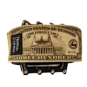 Puede incluir: Un pedal de bicicleta con una envoltura de tela beige que presenta una parodia de un billete de d&oacute;lar. El dise&ntilde;o incluye el texto "THE PERFECT ASS" y "THREE HUNDRED". Una etiqueta negra dice "Pennan Cтрана".