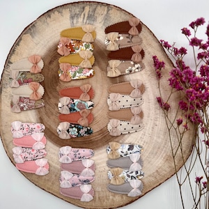 Könnte beinhalten: Ein Set mit 10 Haarklammern mit Blumen- und Tupfenmustern. Die Klammern sind aus Stoff und haben eine braune, beige und rosafarbene Farbgebung.