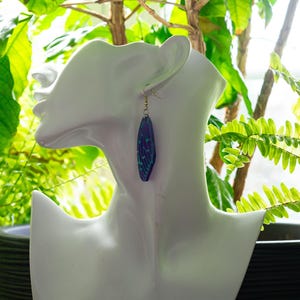 May include: A pair of dangle earrings with a geometric design. The earrings are made of purple and blue resin with a gold-tone hook.