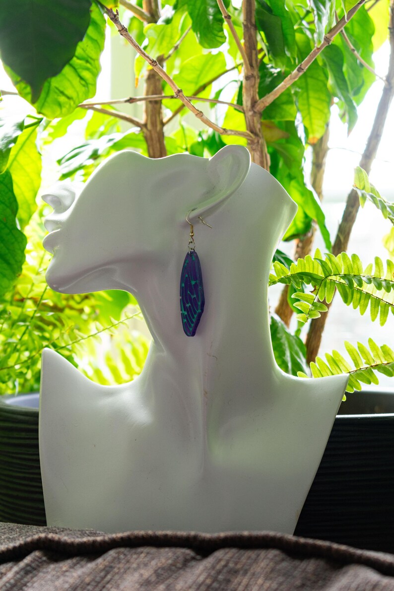 May include: A pair of dangle earrings with a geometric design. The earrings are made of purple and blue resin with a gold-tone hook.