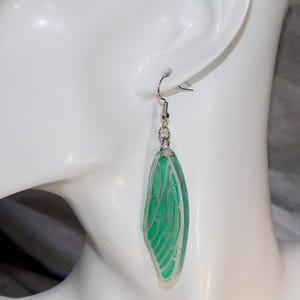 May include: A pair of green dragonfly wing earrings with silver hooks. The wings are translucent and have a delicate vein pattern.