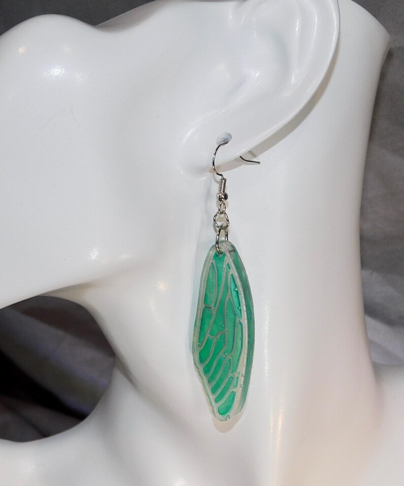 May include: A pair of green dragonfly wing earrings with silver hooks. The wings are translucent and have a delicate vein pattern.