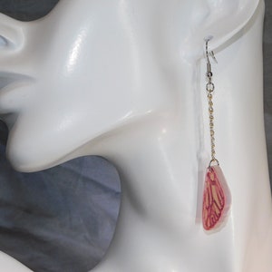 May include: A pair of long, dangling earrings with a delicate gold chain and a pink and white butterfly charm.