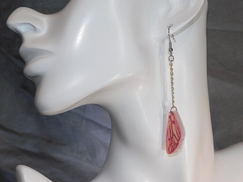 May include: A pair of long, dangling earrings with a delicate gold chain and a pink and white butterfly charm.