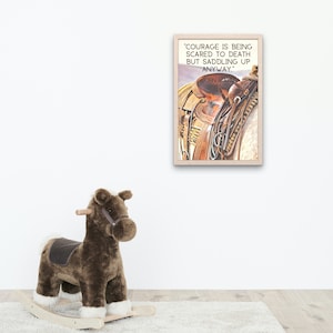 May include: A framed print with the quote "Courage is being scared to death but saddling up anyway." The print features a watercolour image of a horse saddle. A brown rocking horse with white trim is in the foreground.