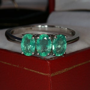 May include: A silver ring with three oval-shaped emerald gemstones set in a row.