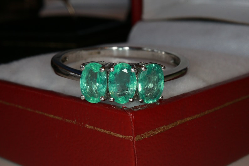 May include: A silver ring with three oval-shaped emerald gemstones set in a row.