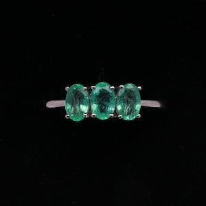 May include: A silver ring with three oval-shaped emerald green gemstones set in a row.