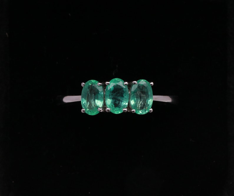 May include: A silver ring with three oval-shaped emerald green gemstones set in a row.