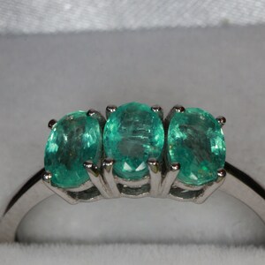 May include: A silver ring with three oval-shaped emerald green gemstones set in the band.