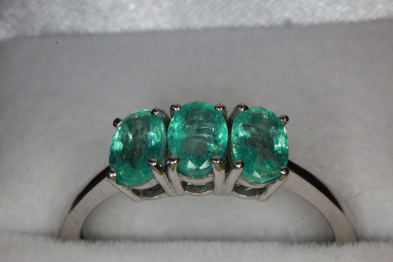May include: A silver ring with three oval-shaped emerald green gemstones set in the band.