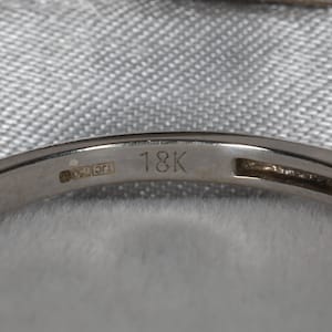 May include: Close-up of the inside of a gold band with the inscription "18K" and a hallmark.