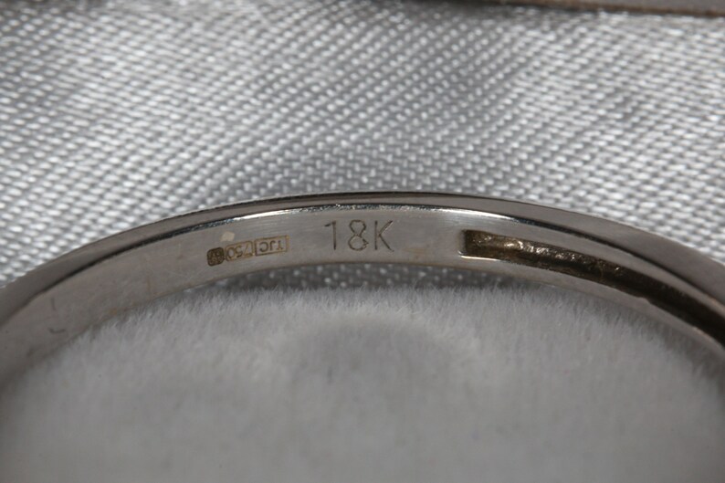 May include: Close-up of the inside of a gold band with the inscription "18K" and a hallmark.