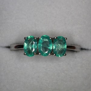 May include: A silver ring with three oval-shaped green gemstones.