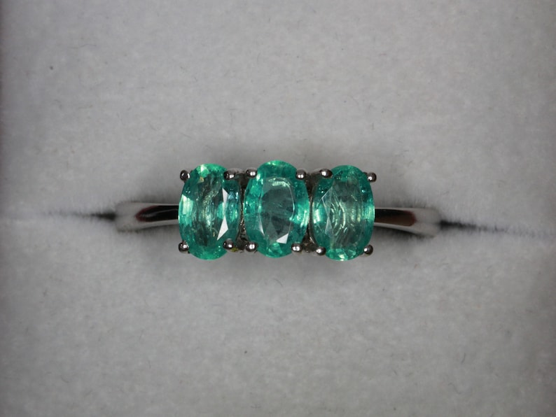 May include: A silver ring with three oval-shaped green gemstones.
