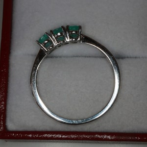 May include: A silver ring with three emerald green gemstones set in a row.