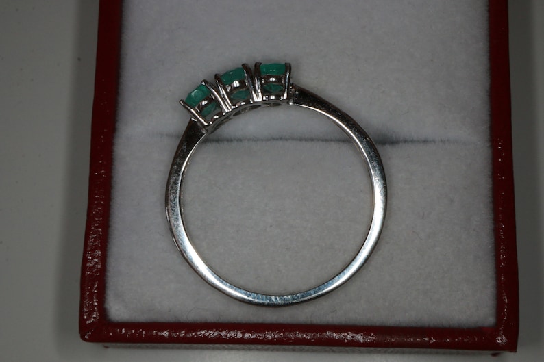 May include: A silver ring with three emerald green gemstones set in a row.