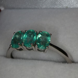 May include: A silver ring with three oval-shaped green gemstones set in a row.