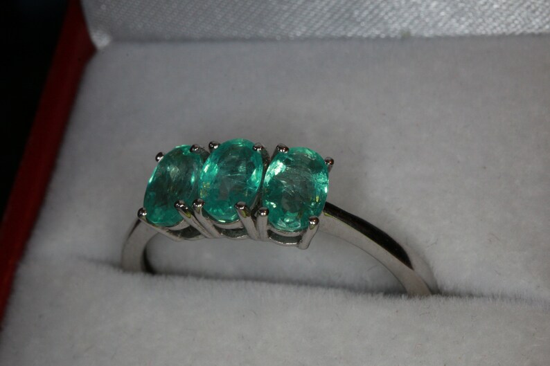May include: A silver ring with three oval-shaped green gemstones set in a row.