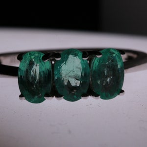 May include: A silver ring with three oval-shaped emerald green gemstones.