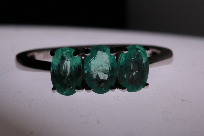 May include: A silver ring with three oval-shaped emerald green gemstones.