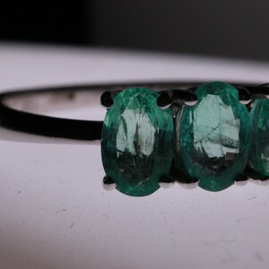 May include: A silver ring with three oval-shaped emerald green gemstones.