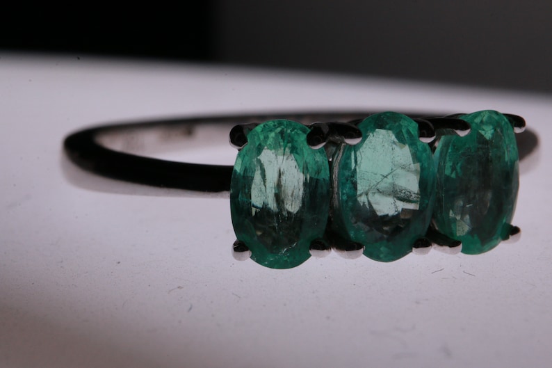 May include: A silver ring with three oval-shaped emerald green gemstones.