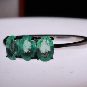 May include: A silver ring with three oval-shaped emerald green gemstones set in a row.