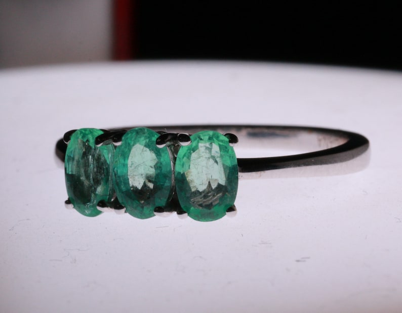 May include: A silver ring with three oval-shaped emerald green gemstones set in a row.